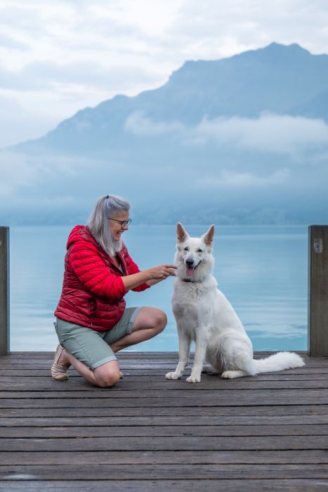 Silvia in Roter Jacke schau rechts neben ihr Jira an. im Hintergrund ein idyllischer See und Berge